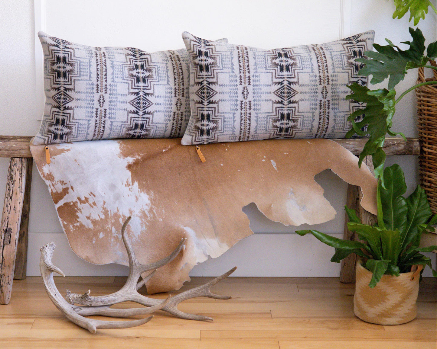 Decorative Pendleton® pillows with geometric patterns on a cowhide rug with antlers, against a white wall.