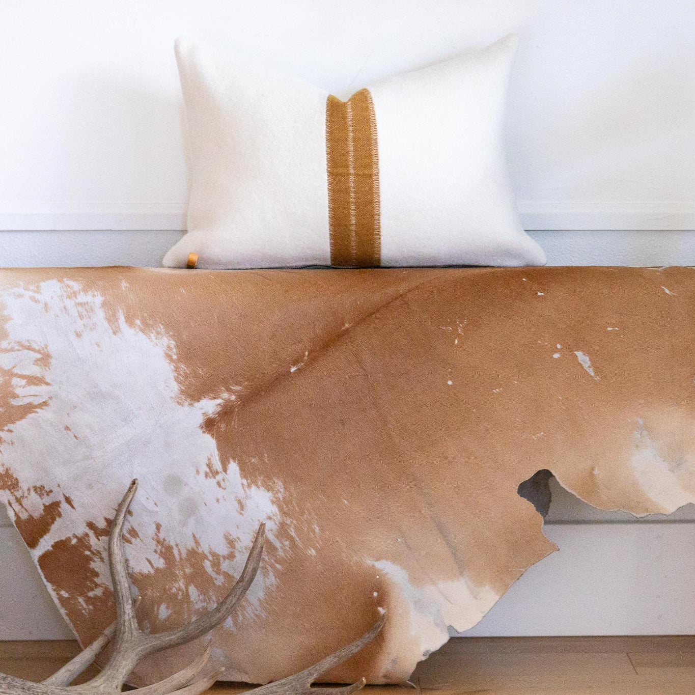 Cowhide rug on a wooden bench with white cushions and a plant in the background