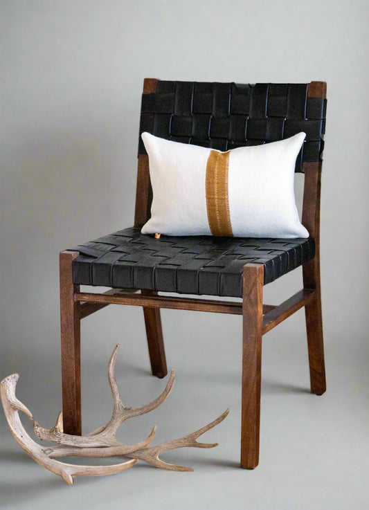Wooden chair with black woven seat and white pillow on a wooden floor with a plant in the background.