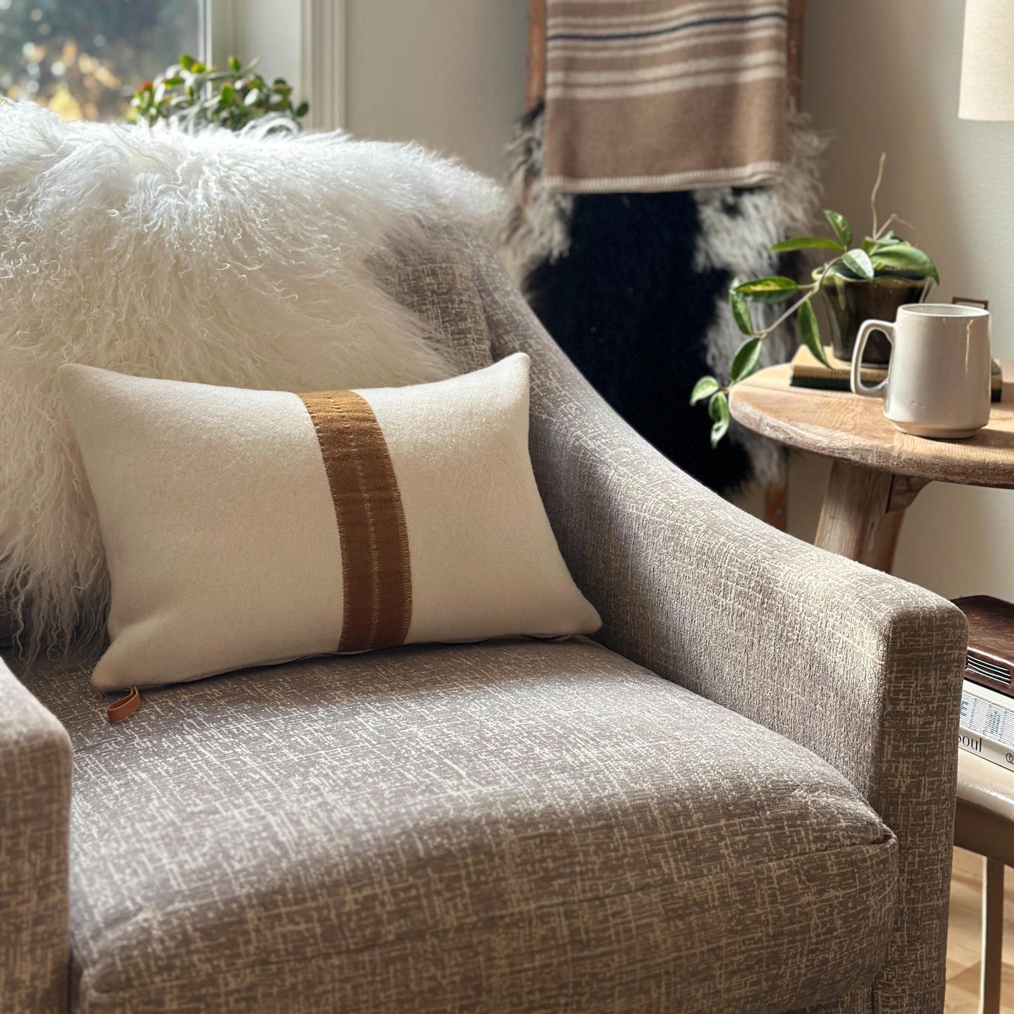Gray armchair with a decorative pillow and a small wooden table with a mug in a cozy living room.