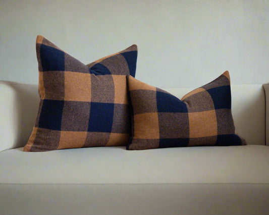 Two checkered pillows on a rustic wooden bench with a white wall and plant in the background.