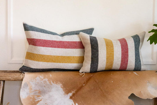 Two striped pillows on a wooden bench with a white wall background