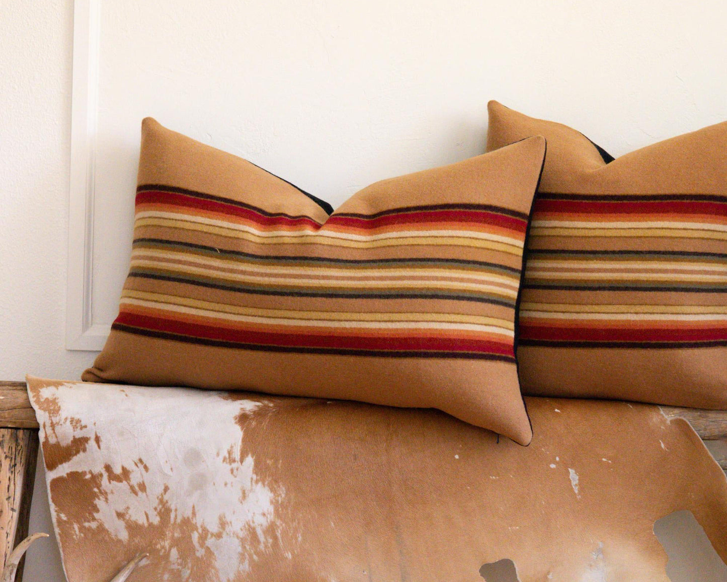 Decorative pillows with striped patterns on a wooden bench with a cowhide rug.