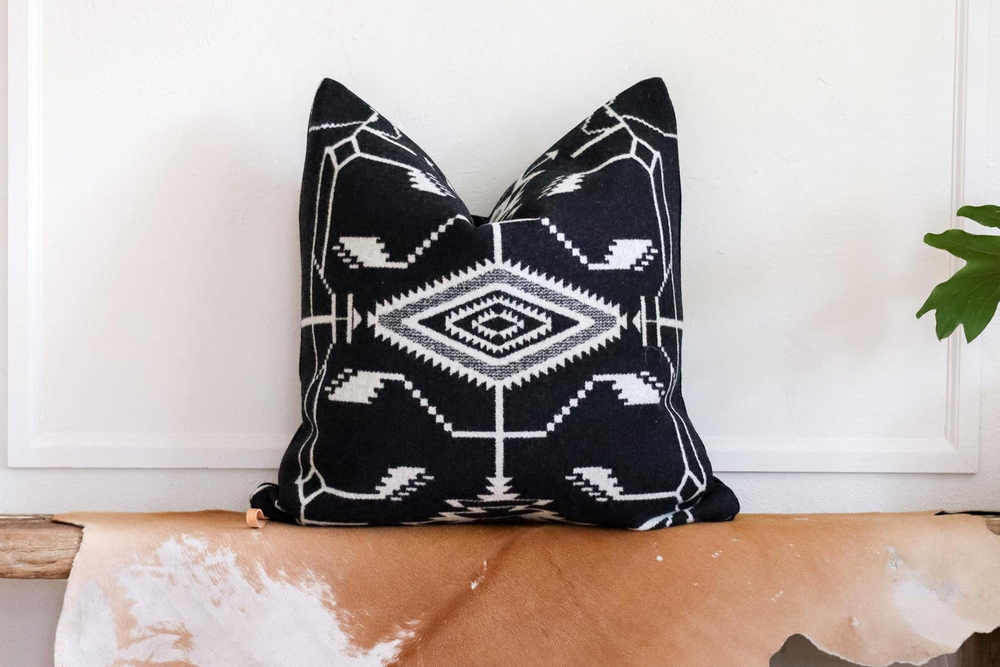 Black and white patterned pillow on a cowhide bench with a white wall background