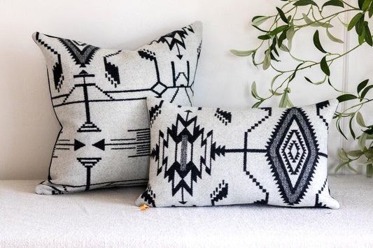 Two decorative pillows with black geometric patterns on a white surface.