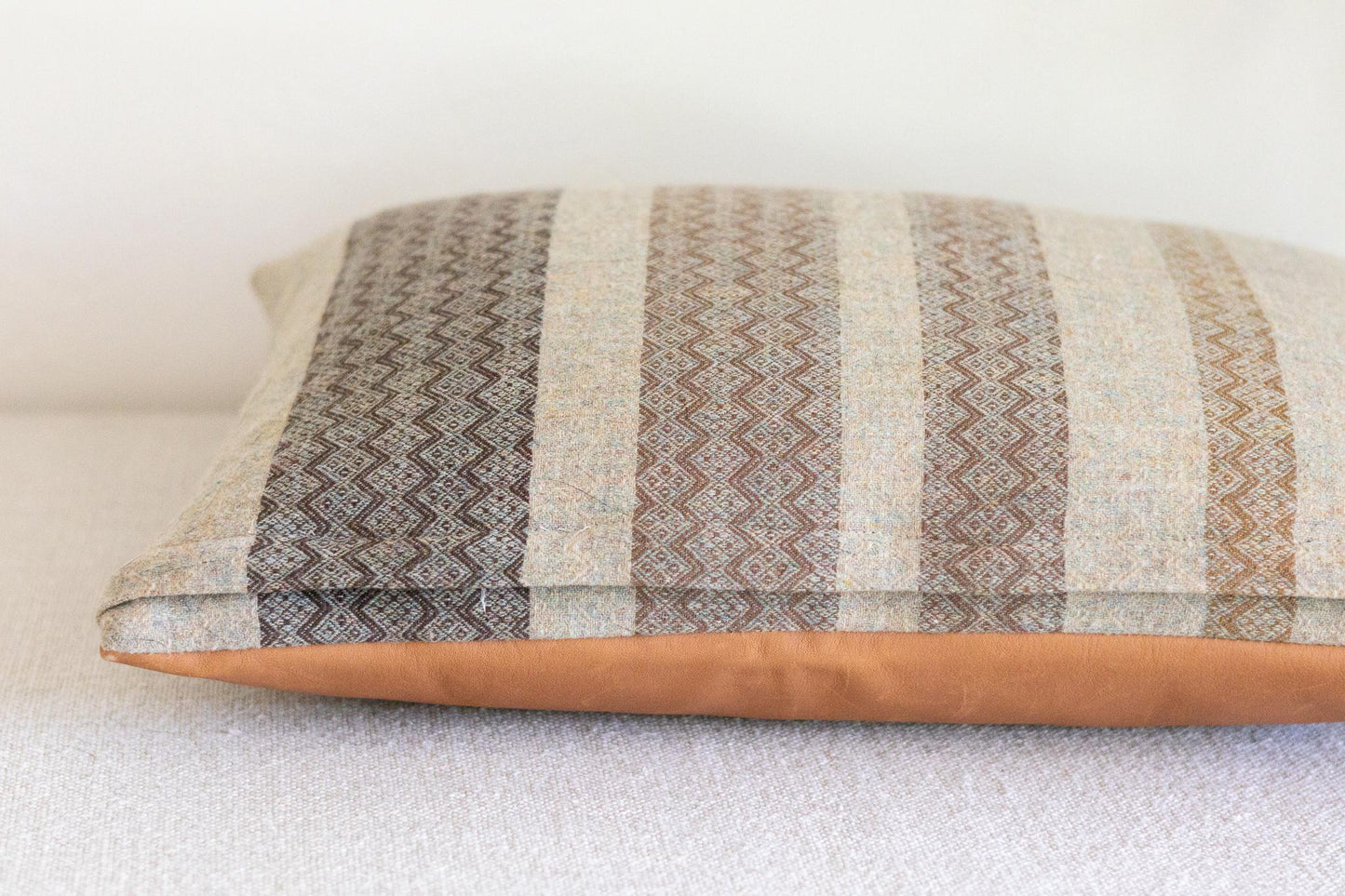 Decorative pillow with striped pattern and leather trim on a white background