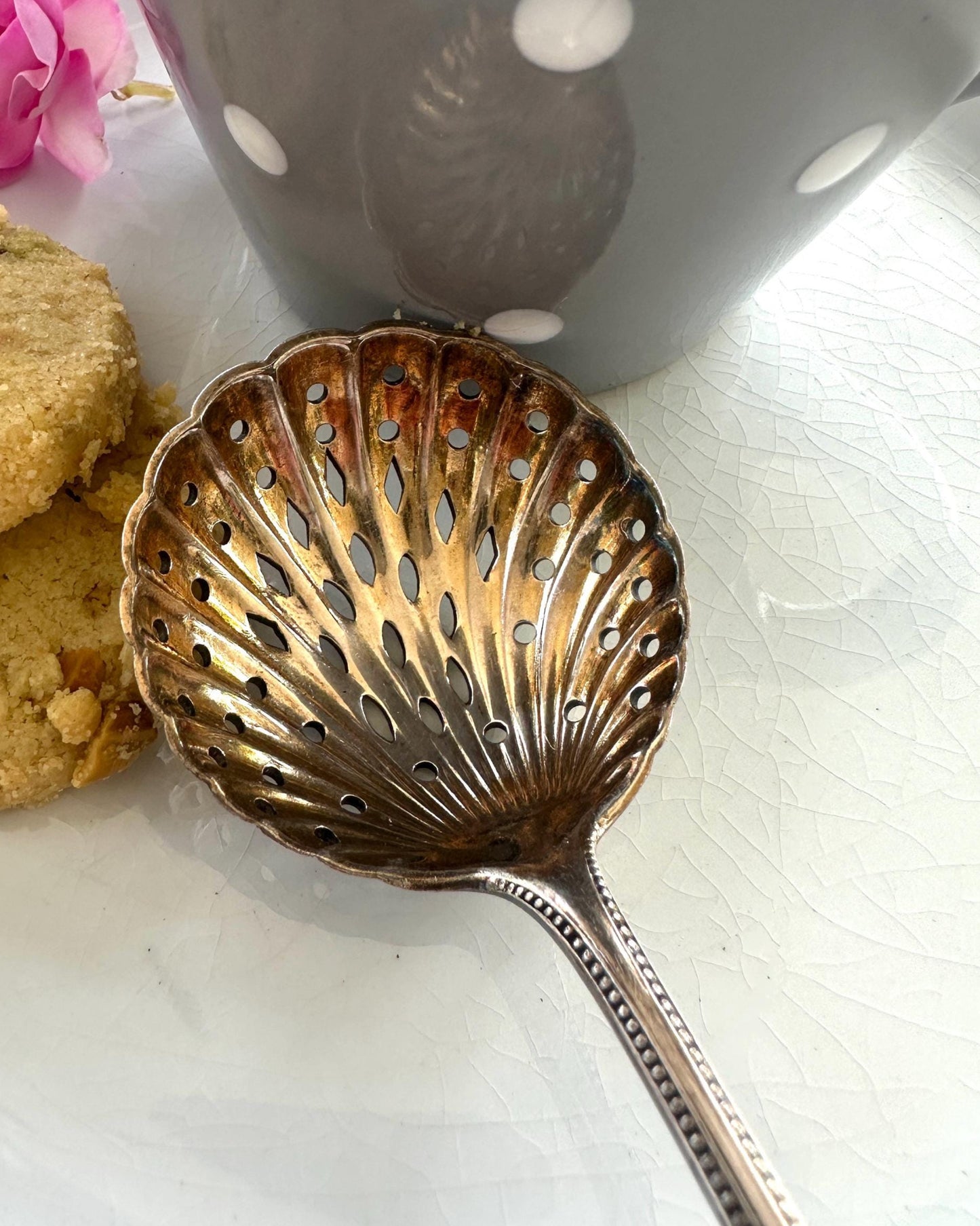 Antique sugar-sifter spoon with cookies and a mug on a white surface