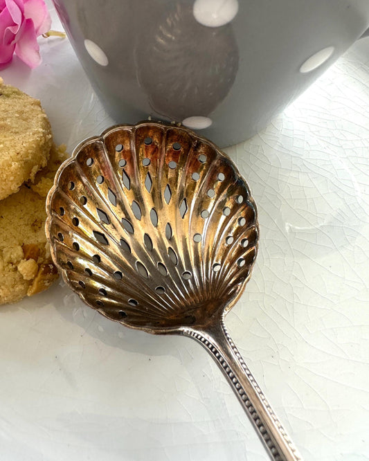 Antique sugar-sifter spoon with cookies and a mug on a white surface
