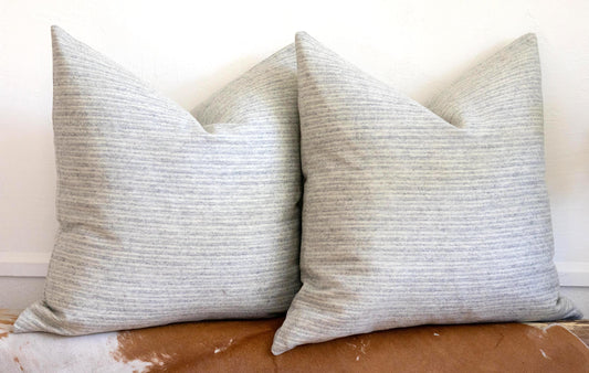 Two gray textured pillows on a brown leather couch against a white wall.