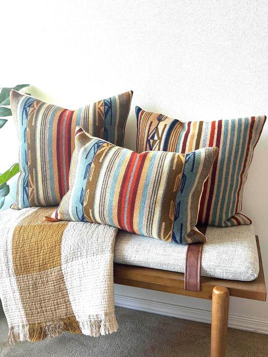 Colorful striped pillows on a wooden bench with a white wall background