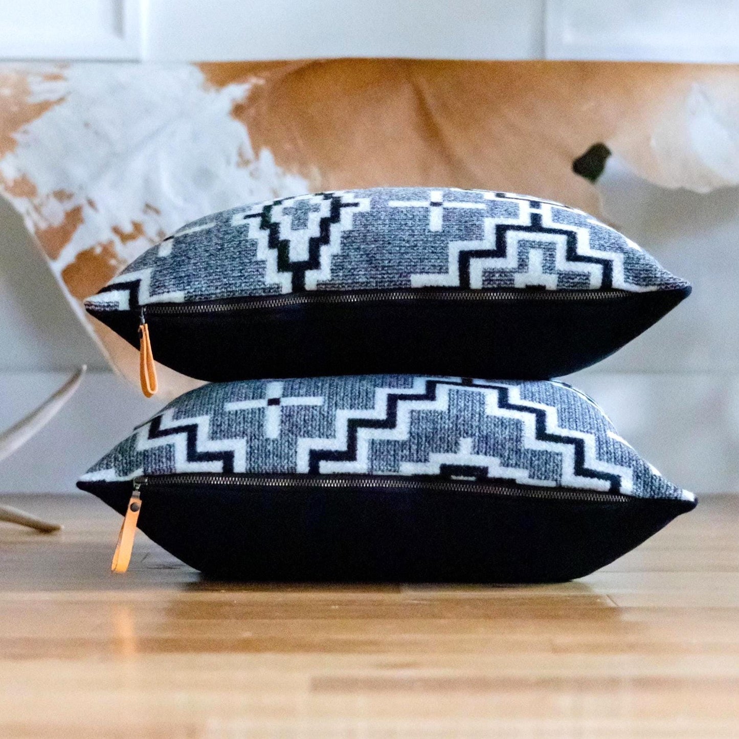 Two black and white patterned pouches stacked on a wooden surface with a blurred background.