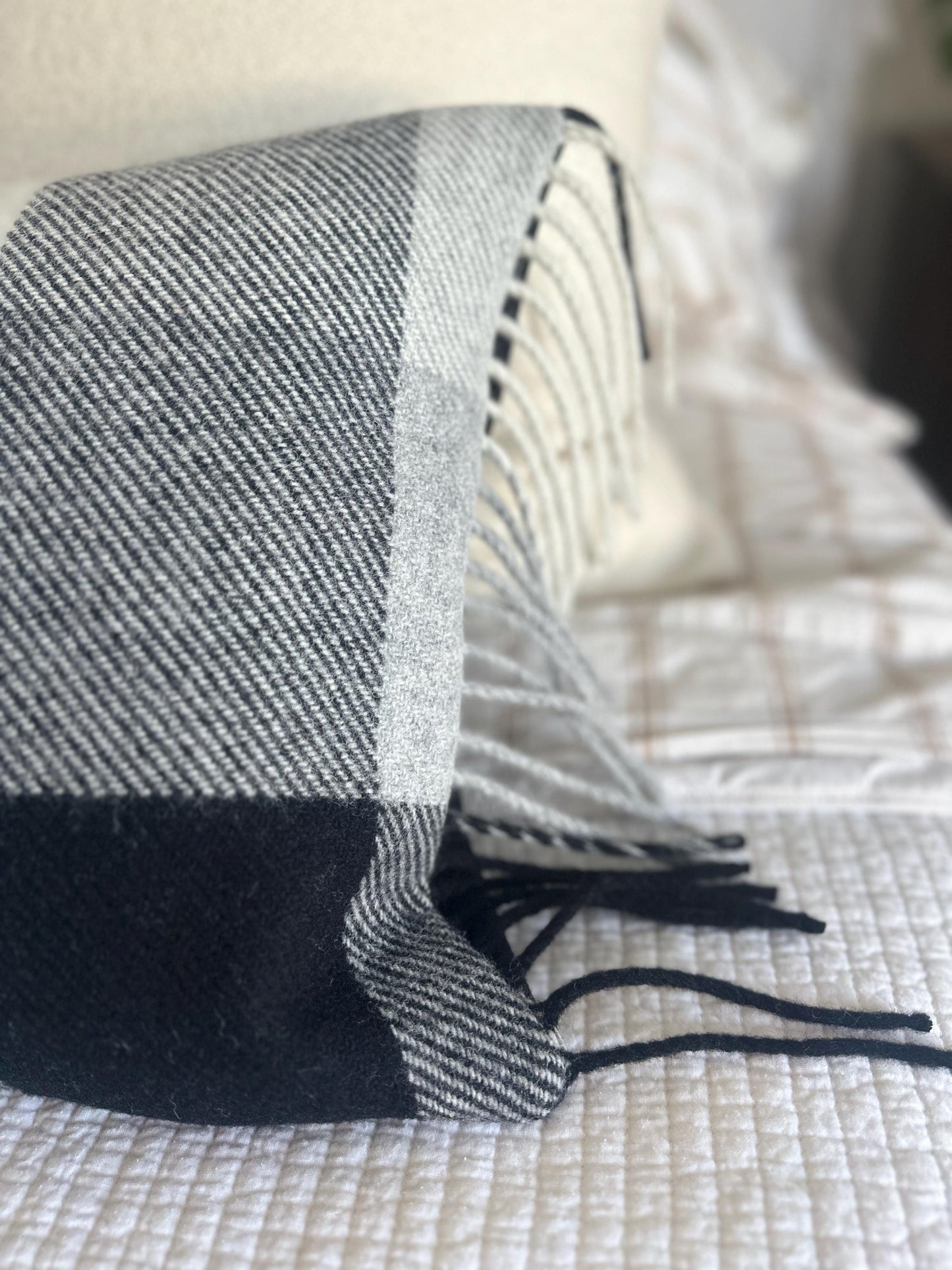 Gray and black checkered pillow with tassels on a textured surface