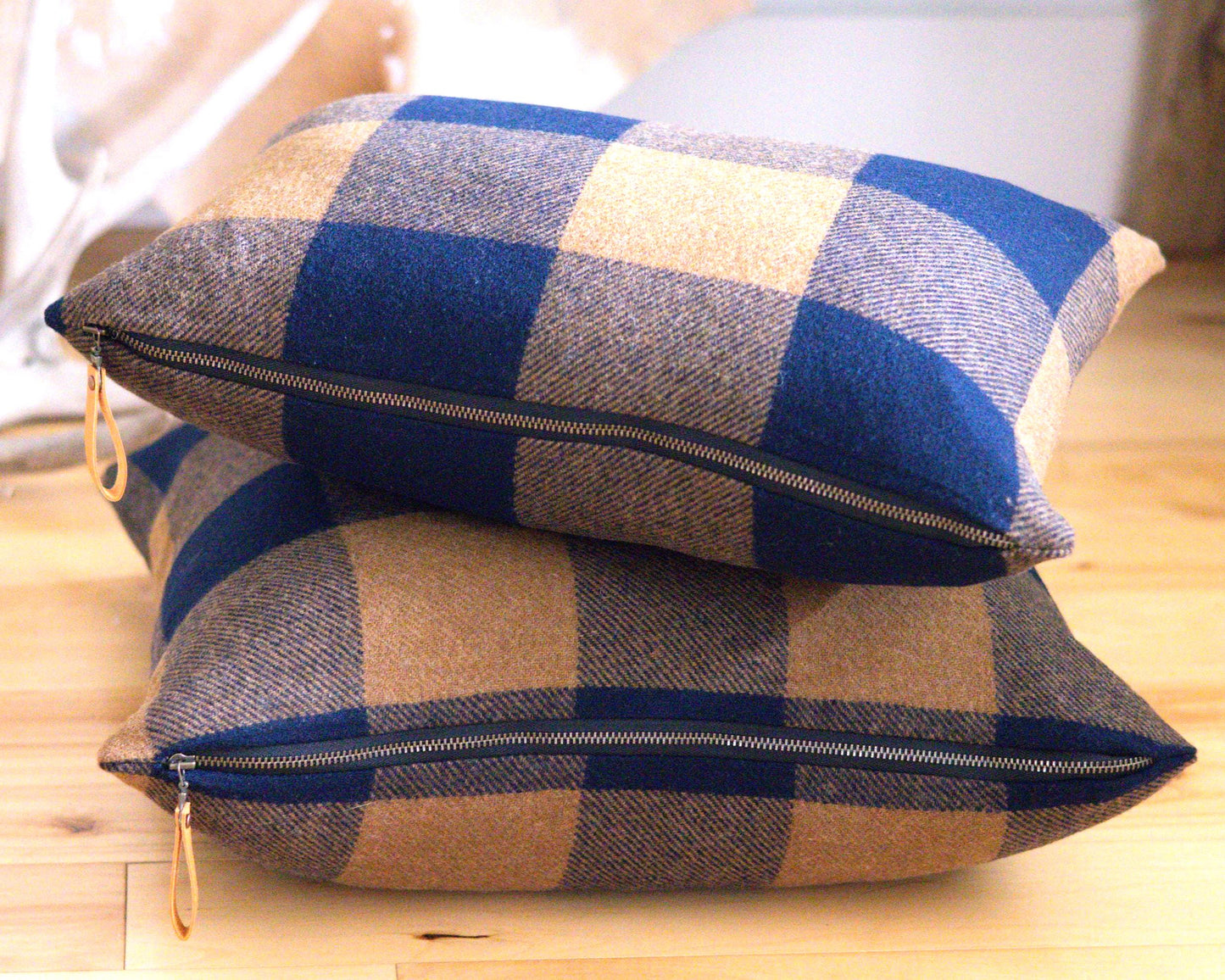 Two buffalo check patterned pillows with zippers on a wooden surface.