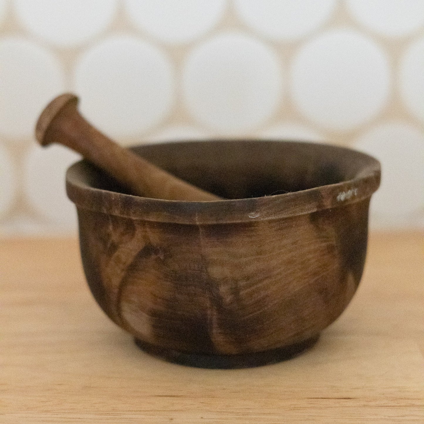 Wooden mortar and pestle on a wooden surface with a white tiled wall background
