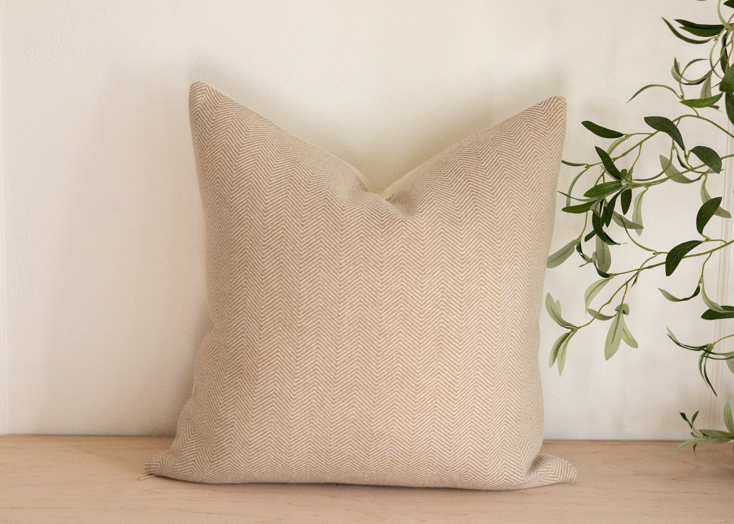 Beige textured pillow on a wooden surface with a plant in the background