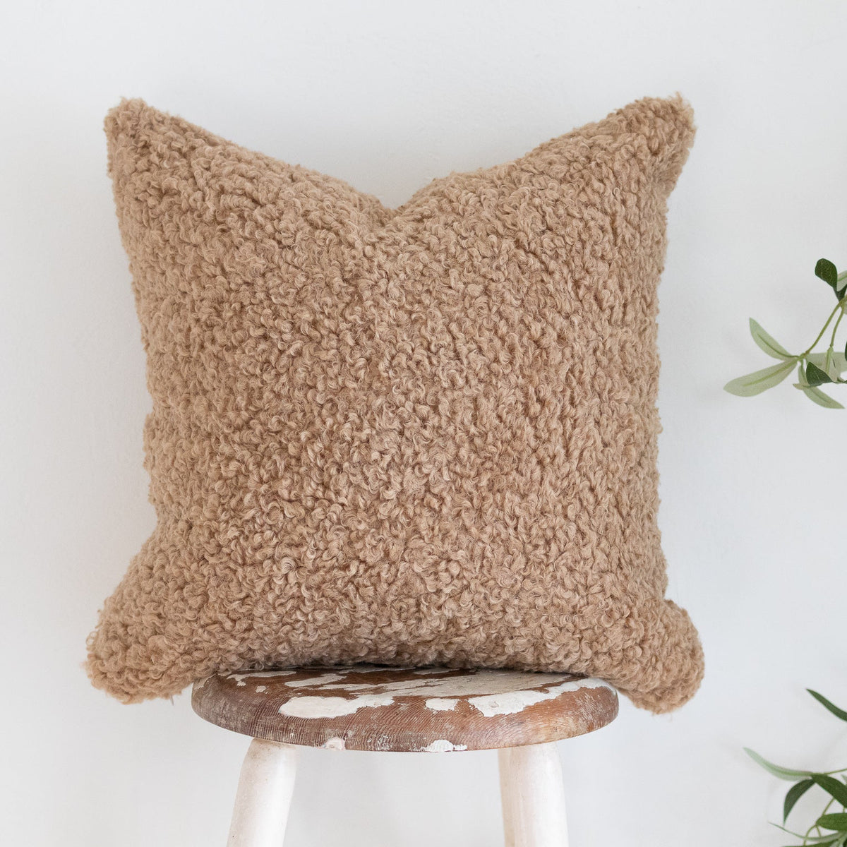 Brown textured pillow on a white stool with a plant in the background