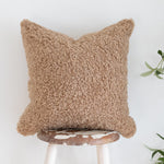 Brown textured pillow on a white stool with a plant in the background