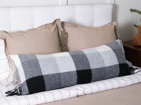 Plaid body pillow on a bed with beige pillows