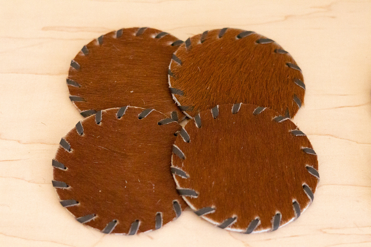 Four brown leather coasters with metal edges on a wooden surface