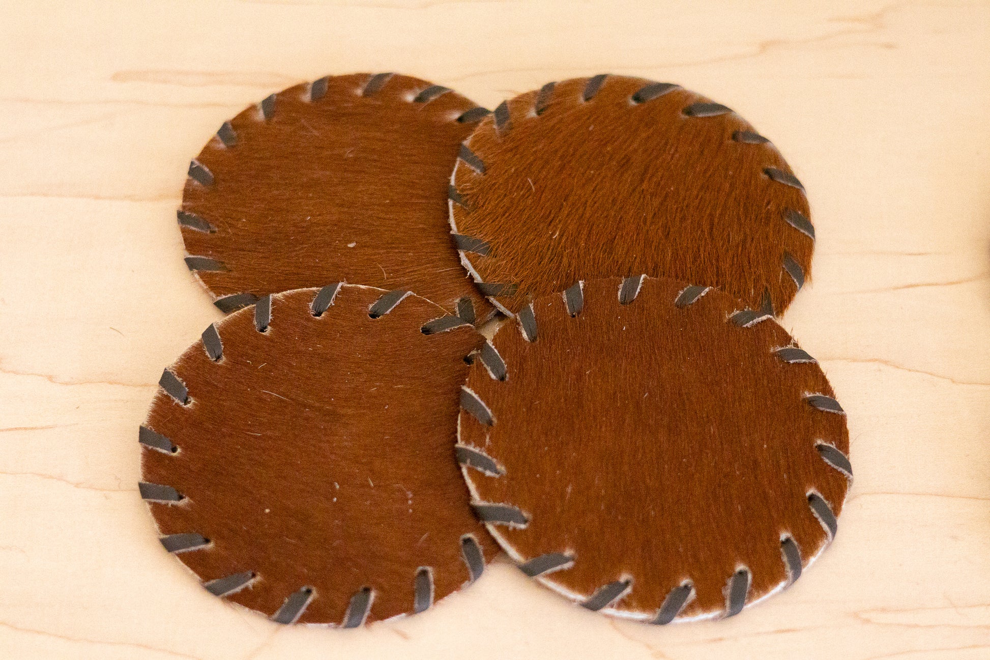 Four brown leather coasters with metal edges on a wooden surface