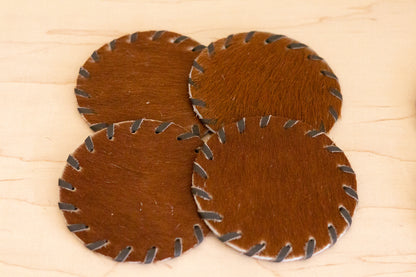 Four brown leather coasters with metal edges on a wooden surface