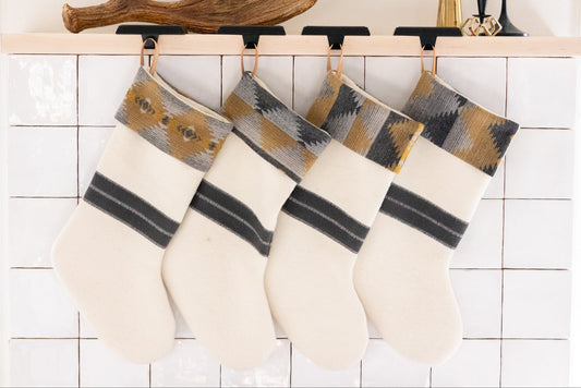 Set of four white Christmas stockings with patterned tops hanging on a fireplace mantle.