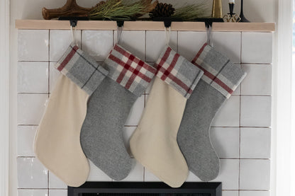Four Christmas stockings with plaid trim hanging on a fireplace mantle.