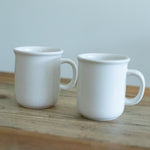 Two white ceramic mugs on a wooden surface with a light gray background