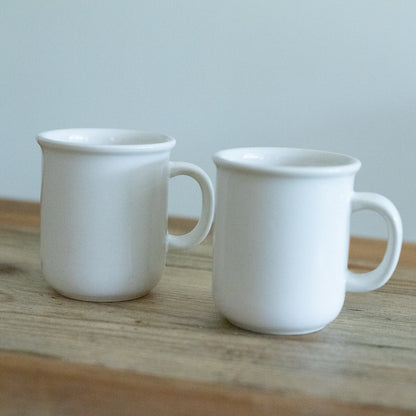 Two white ceramic mugs on a wooden surface with a light gray background