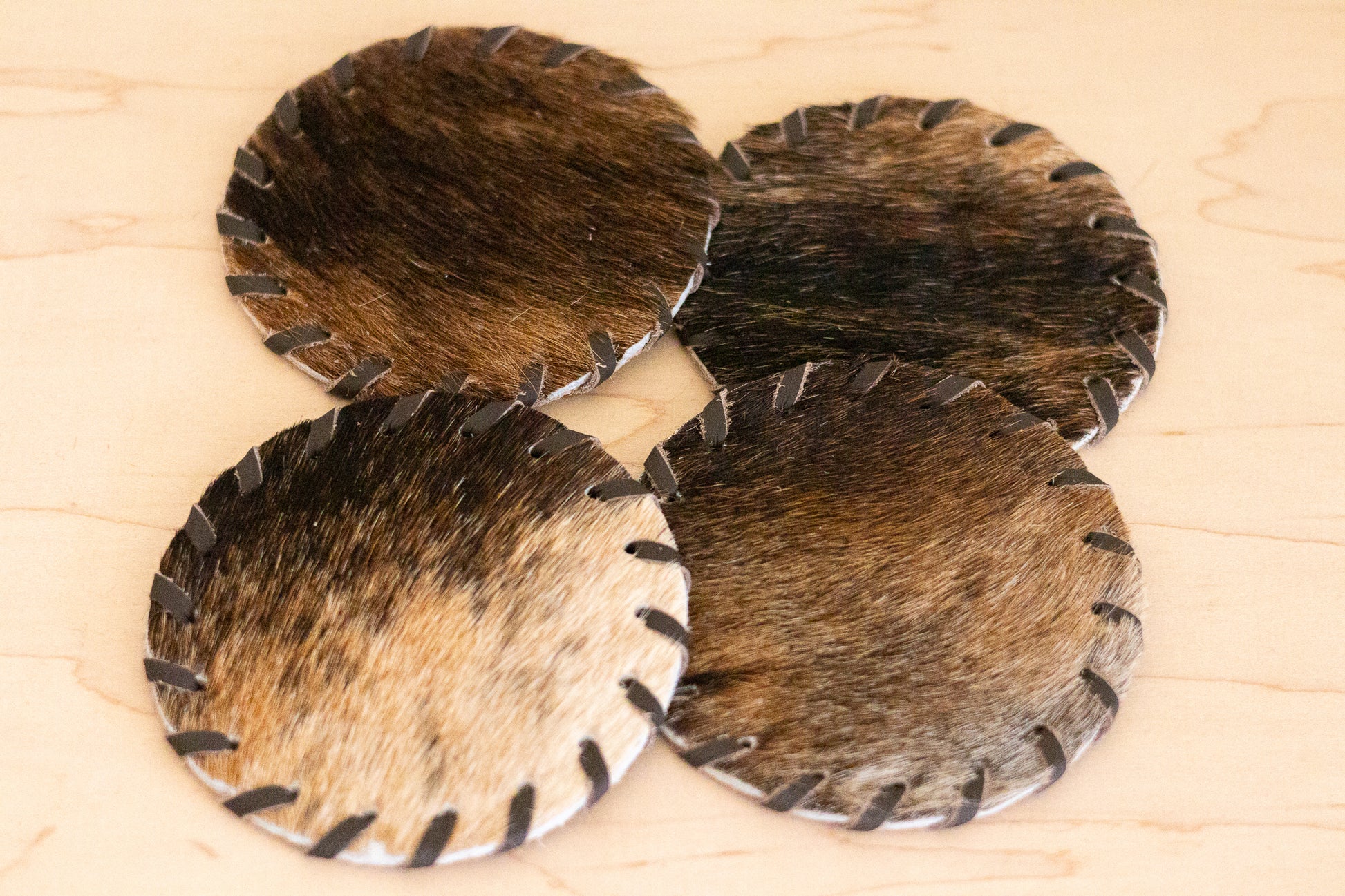 Four round cowhide coasters with metal rims on a wooden surface