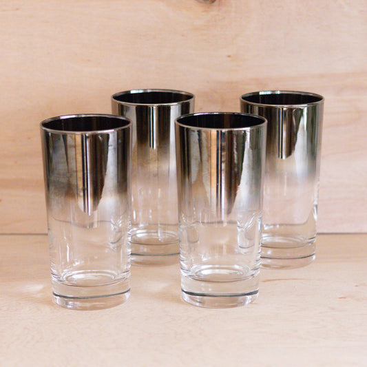 Four clear glass tumblers with metallic rim on a wooden surface
