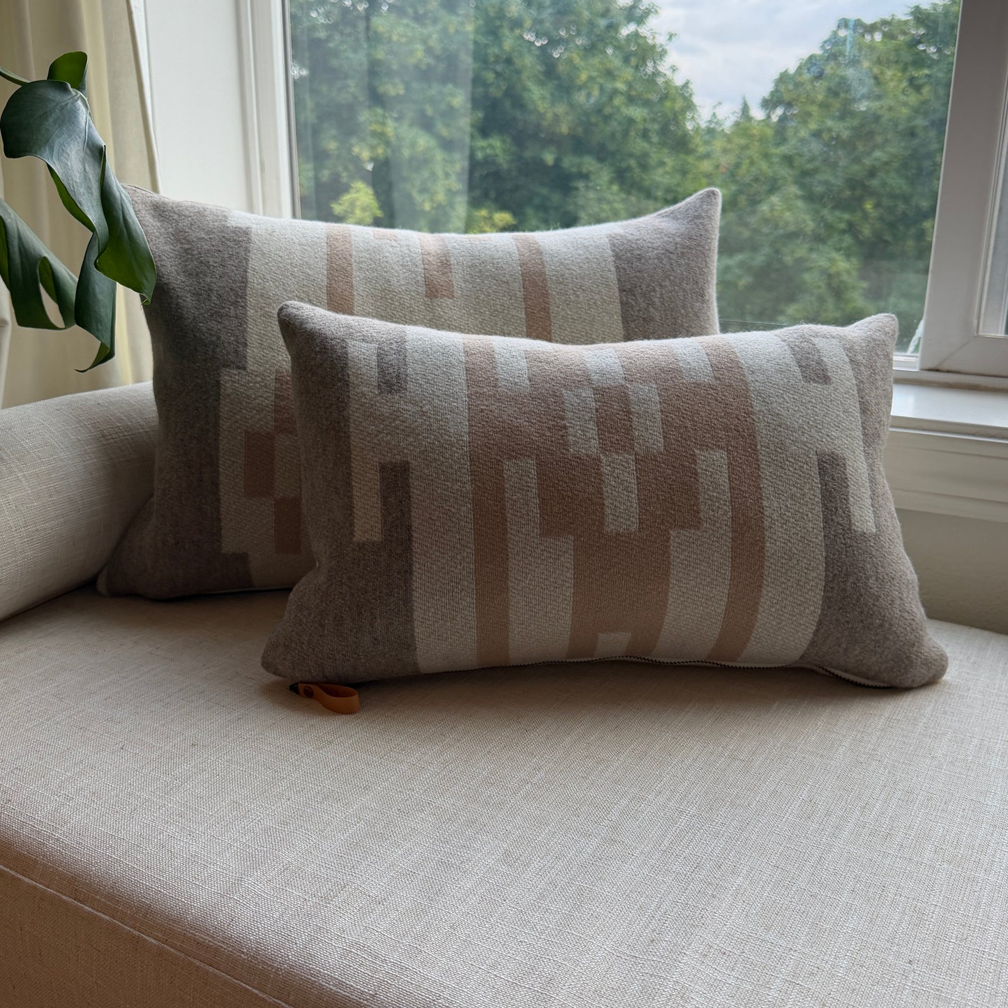 Two patterned cushions on a light-colored sofa next to a window with a view of trees.