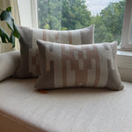 Two patterned cushions on a light-colored sofa next to a window with a view of trees.