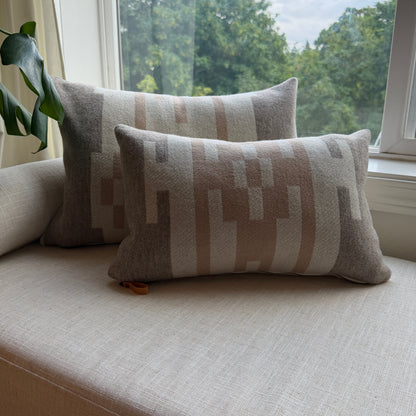 Two patterned cushions on a light-colored sofa next to a window with a view of trees.