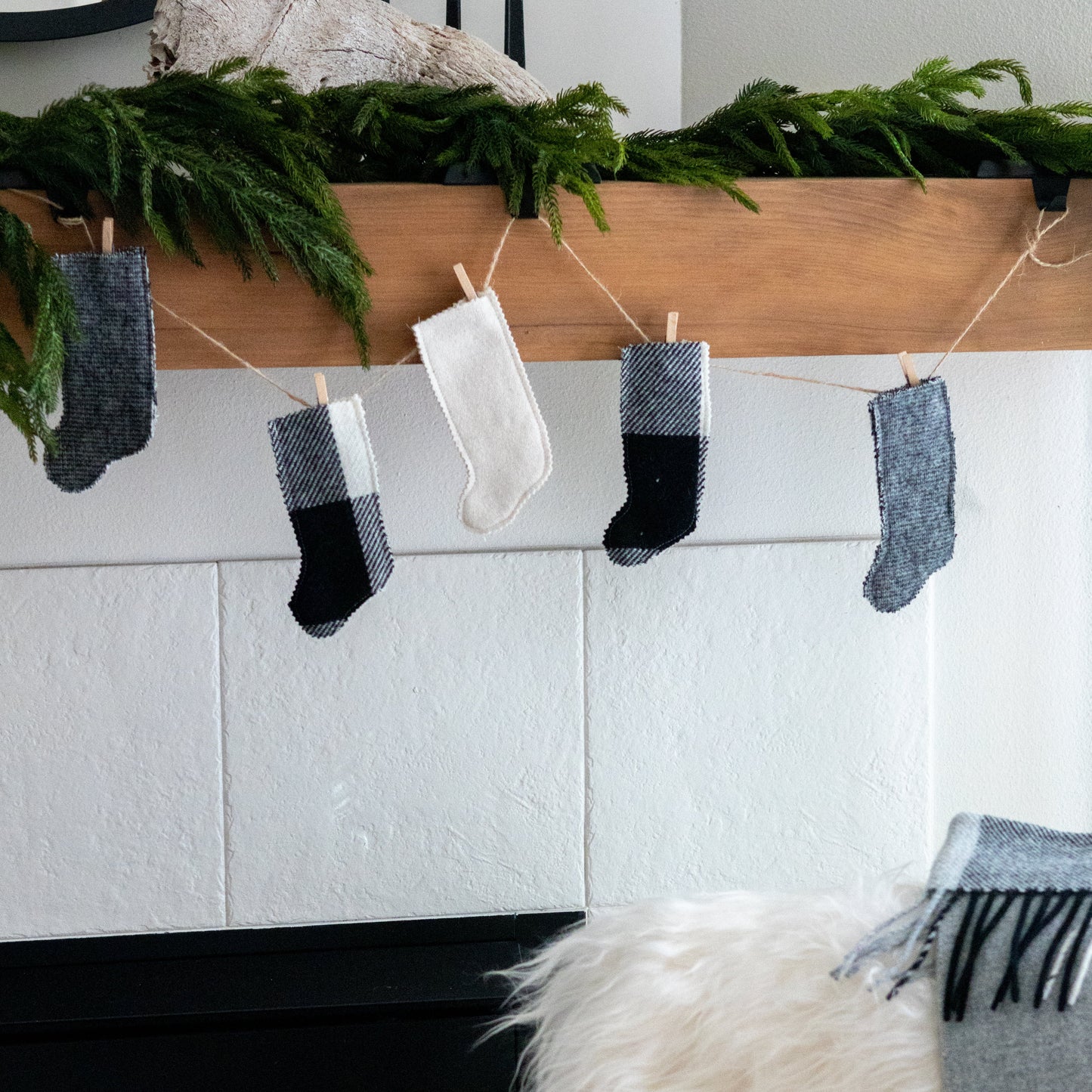 Decorative stockings hanging above a fireplace with a mantel decorated with greenery.
