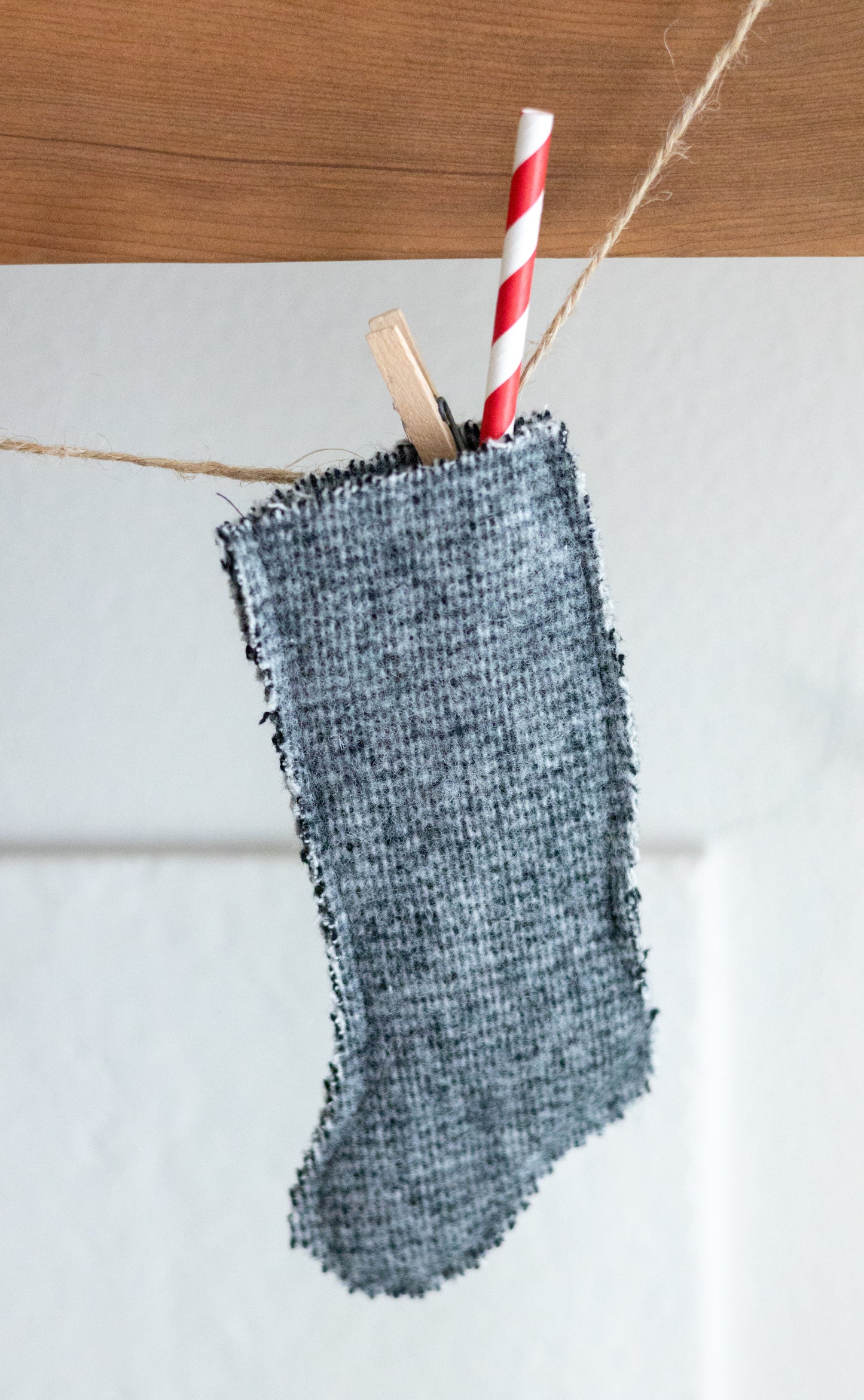 Green wool textured stocking with a red and white striped straw hanging on a wooden surface.