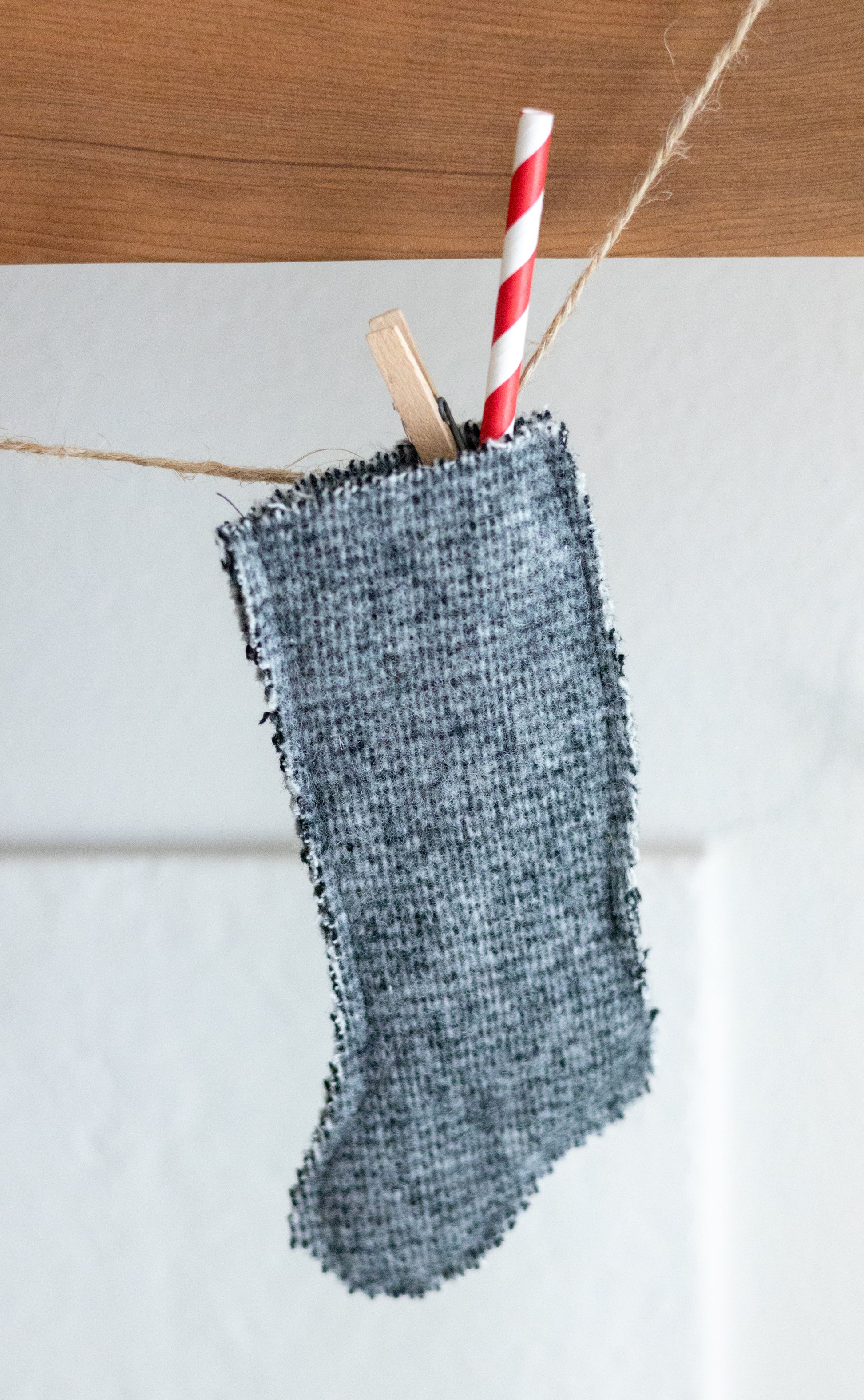 Green wool textured stocking with a red and white striped straw hanging on a wooden surface.