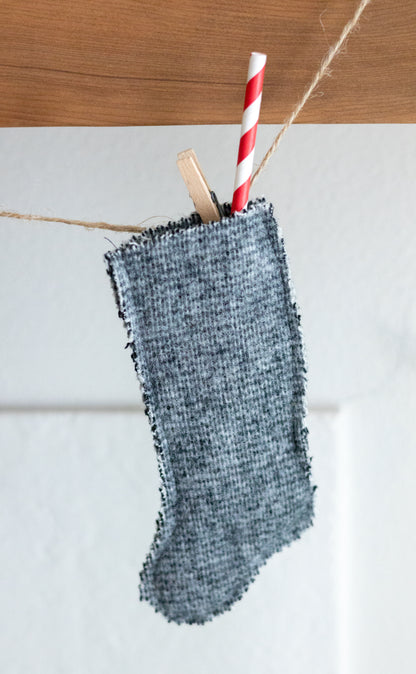 Green wool textured stocking with a red and white striped straw hanging on a wooden surface.