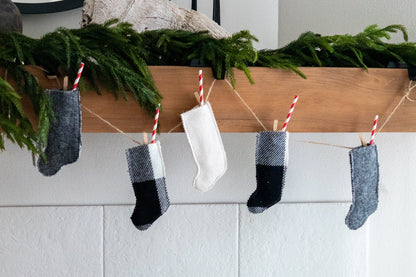 Miniature Christmas stockings hanging on a line with greenery above, against a white wall.