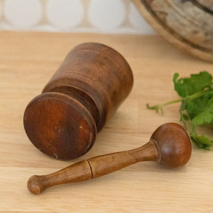 Wooden mortar and pestle on a wooden surface with herbs in the background