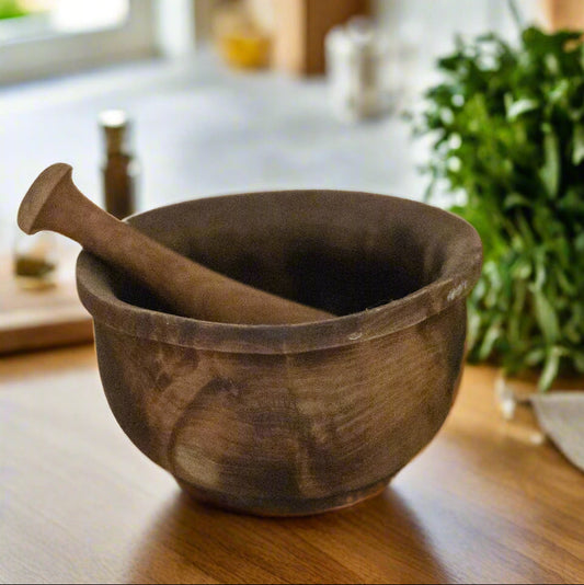 Wooden mortar and pestle on a wooden surface with herbs in the background