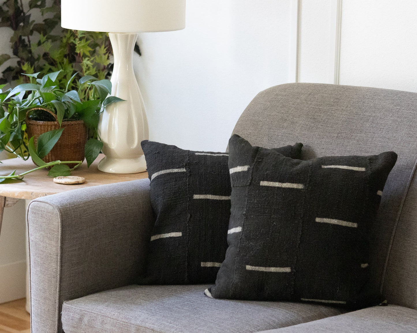 Gray sofa with dark patterned cushions, side table with plant and lamp, white wall background