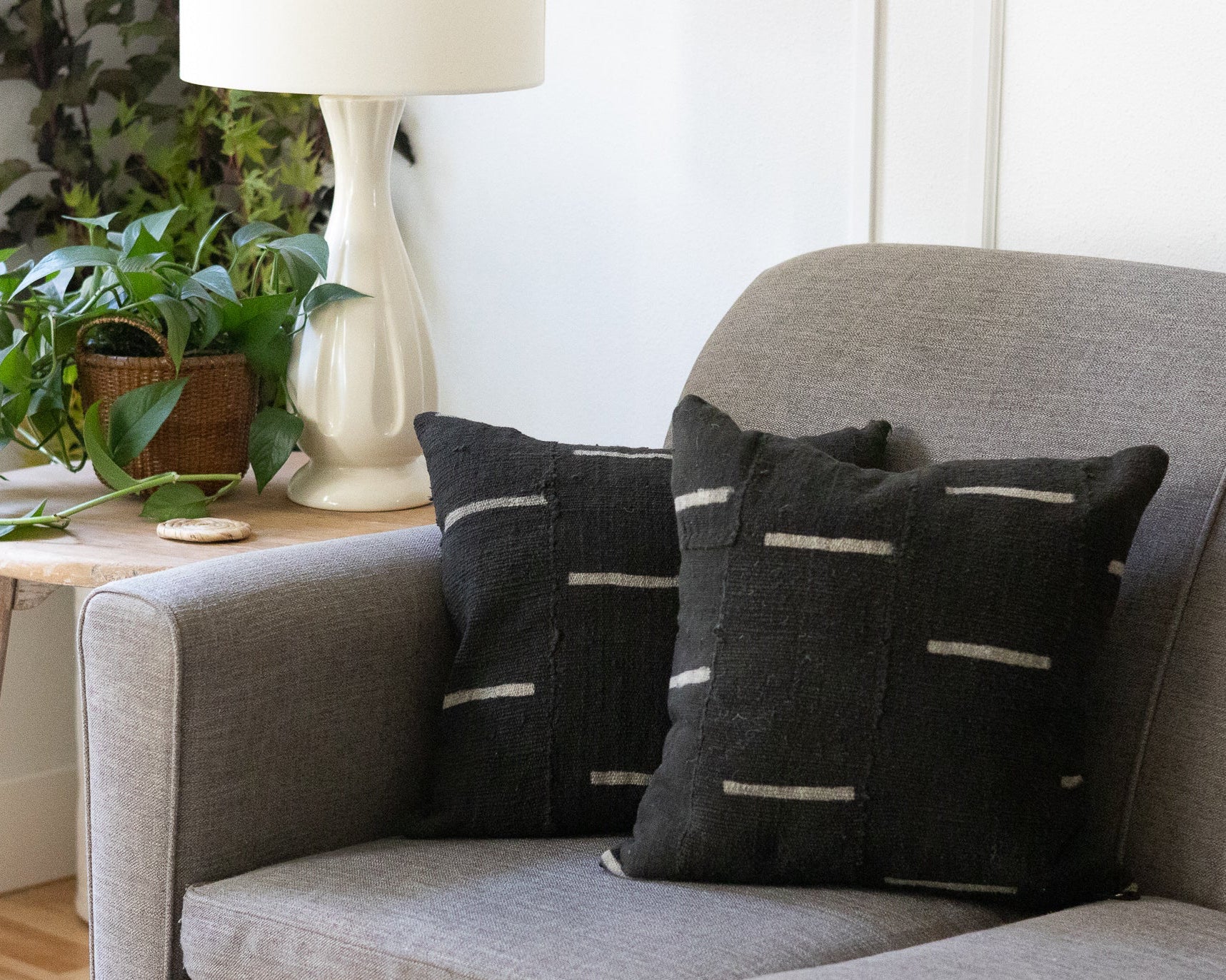 Gray sofa with dark patterned cushions, side table with plant and lamp, white wall background