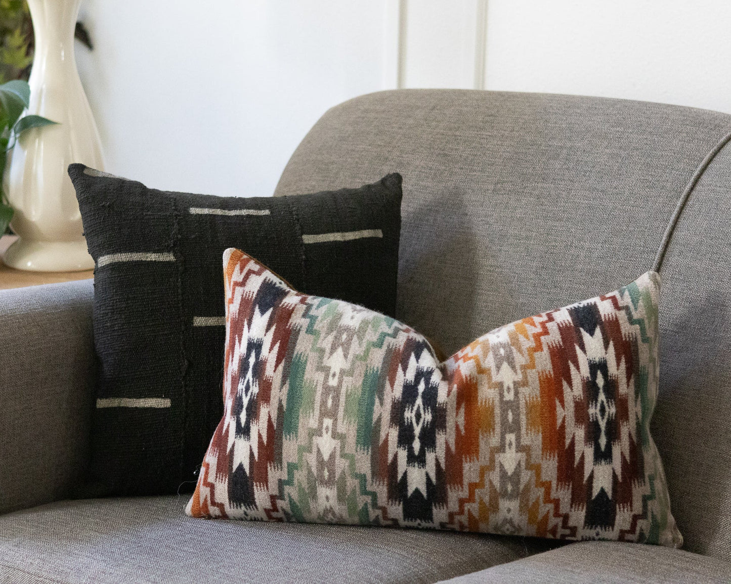 Decorative pillows on a gray sofa with a plant and vase in the background