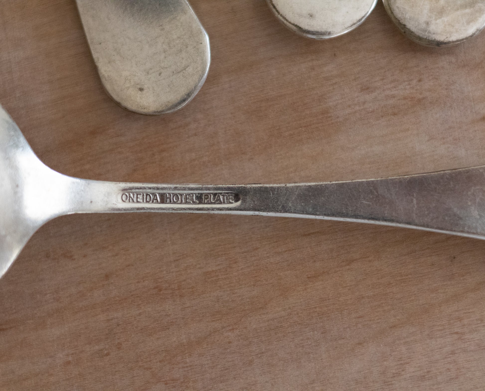 Close-up of a silver spoon with 'Oneida Hotel & Club' engraving on a wooden surface.