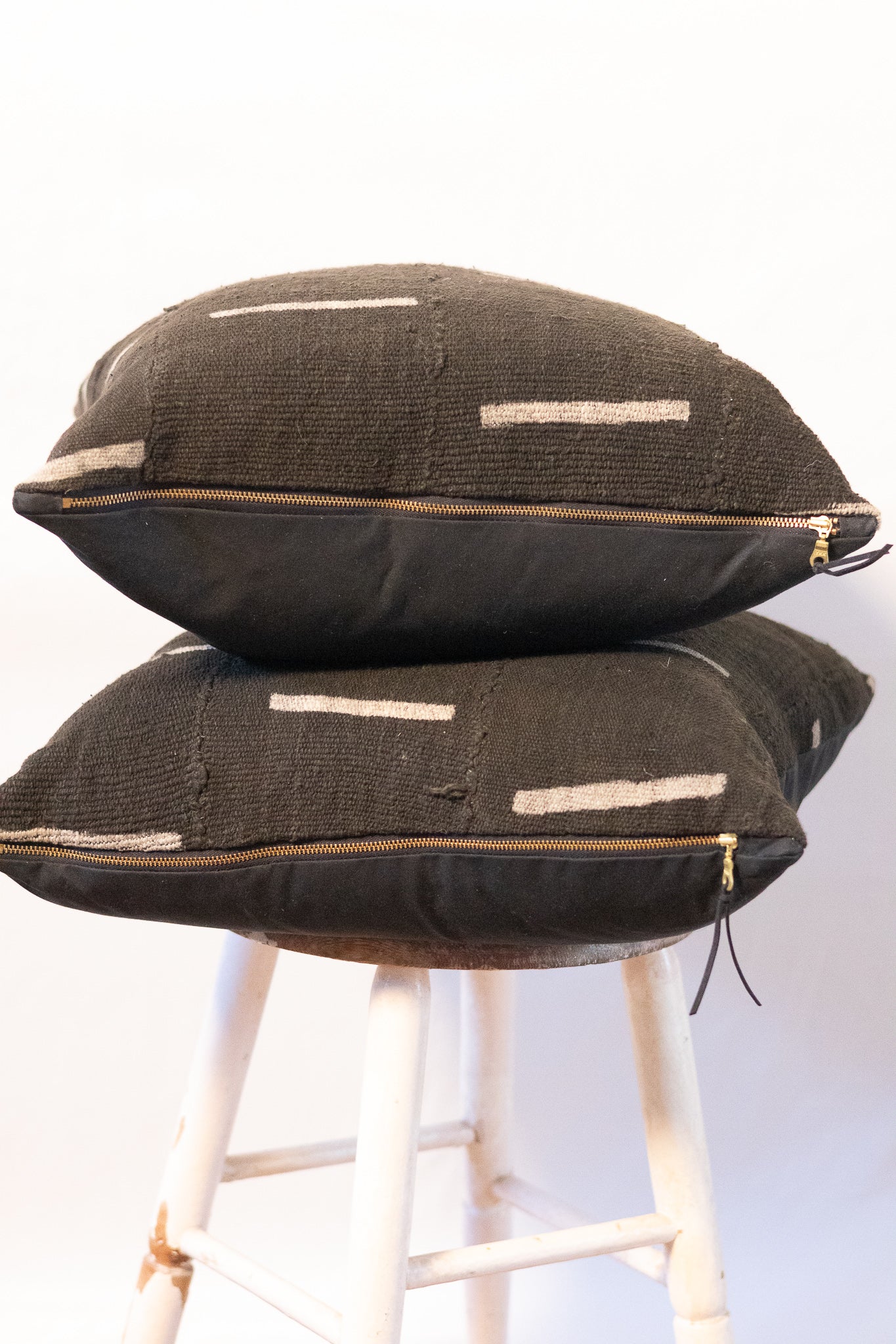 Two black textured pillows stacked on a white stool against a white background