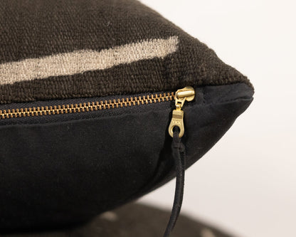 Close-up of a black pillow with a gold zipper on a neutral background