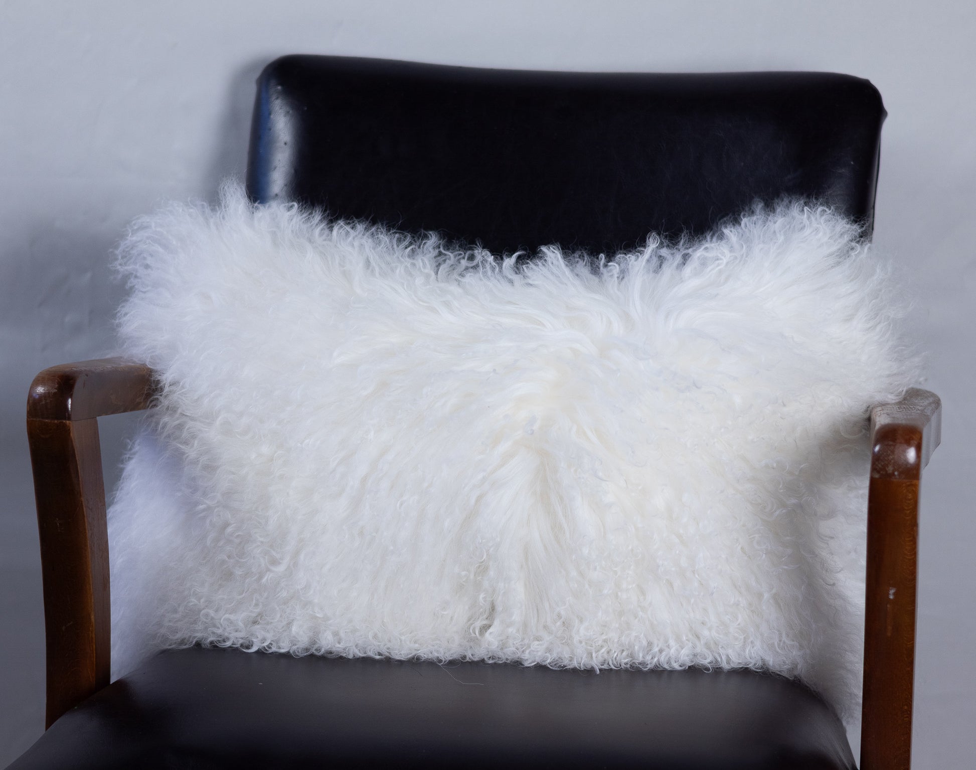 White fluffy pillow on a black chair against a gray background