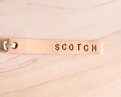 Leather tag with 'SCOTCH' engraving on a wood background