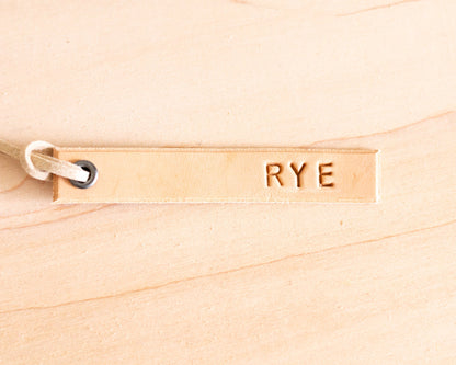Close-up of a beige leather strap with 'RYE' branding on a matching wood background.